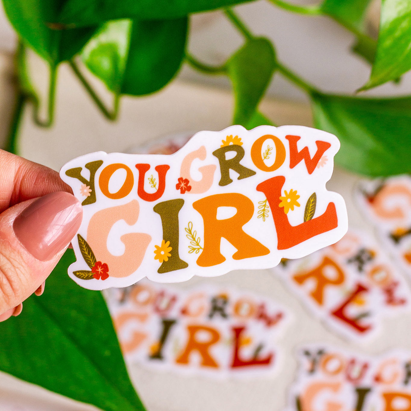 Woman holding a You Grow Girl Vinyl Sticker in front of plants