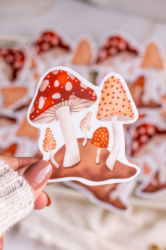 Woman holding a Forest Mushroom Vinyl Sticker in front of other mushroom stickers behind it