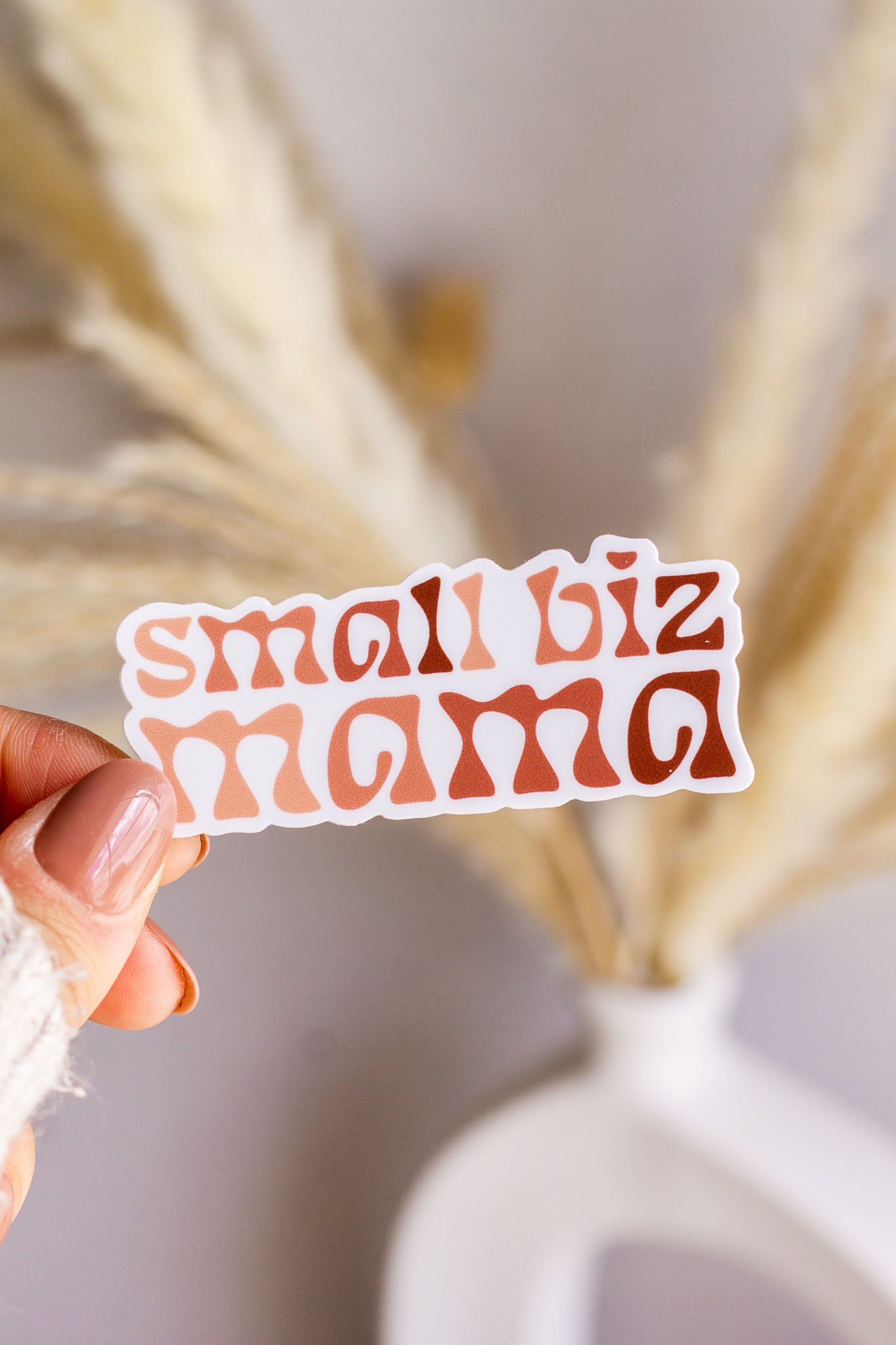 Woman holding a Small Biz Mana Vinyl Sticker with dried flowers in the background