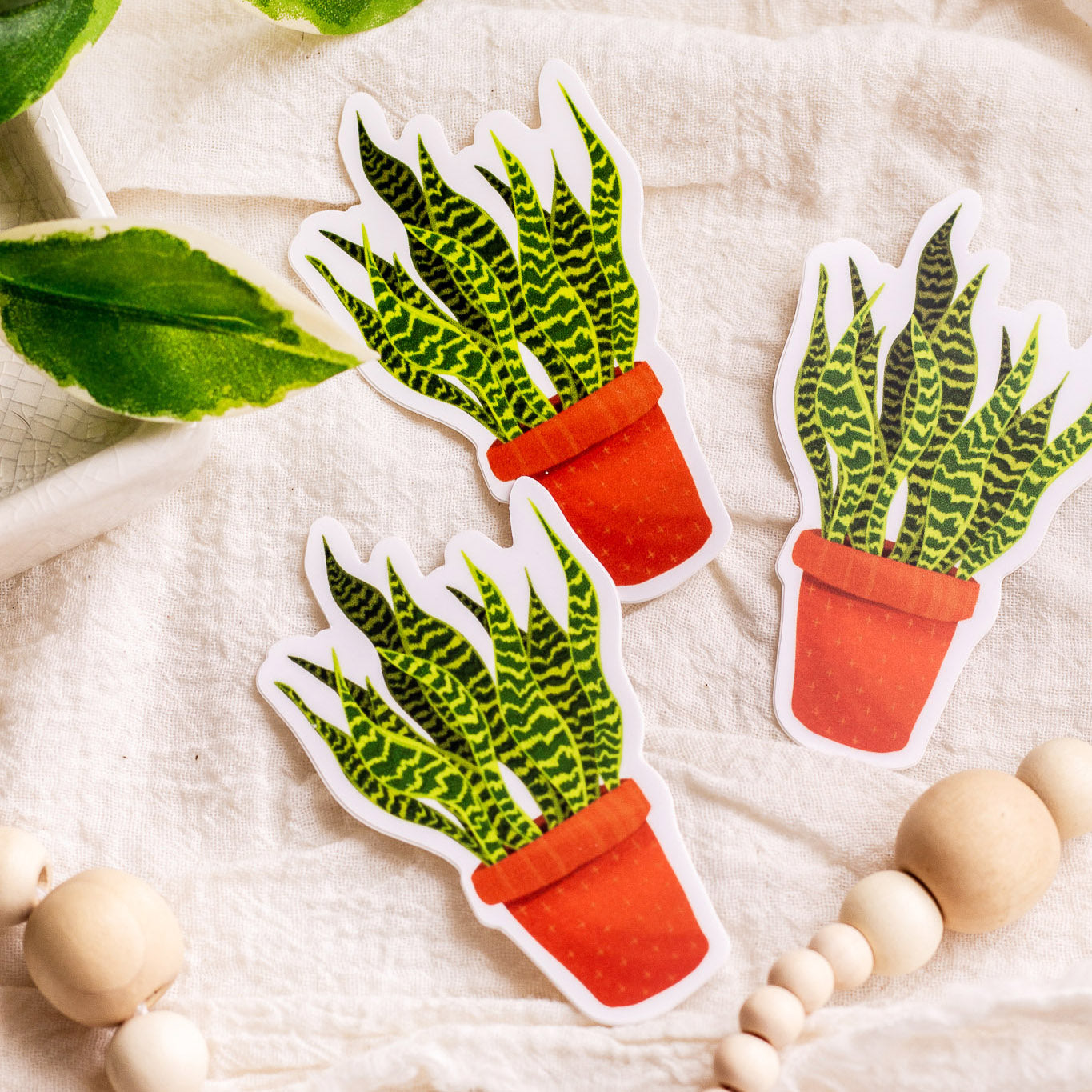 Snake Plant Vinyl Stickers laying on decorative fabric with greenery next to them