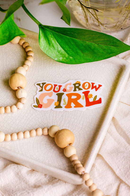 You Grow Girl Vinyl Sticker laying on a decorative tray with houseplants next to it